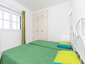 Une chambre avec deux lits, une fenêtre avec des rideaux, une armoire et une lampe de chevet.