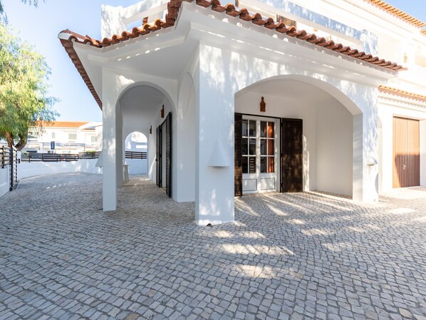 A building with white walls and a tiled roof, featuring a covered outdoor area with a cobblestone floor and a wooden fence. - Branle Villa, Wifi, Near Beach (Manta Rota)