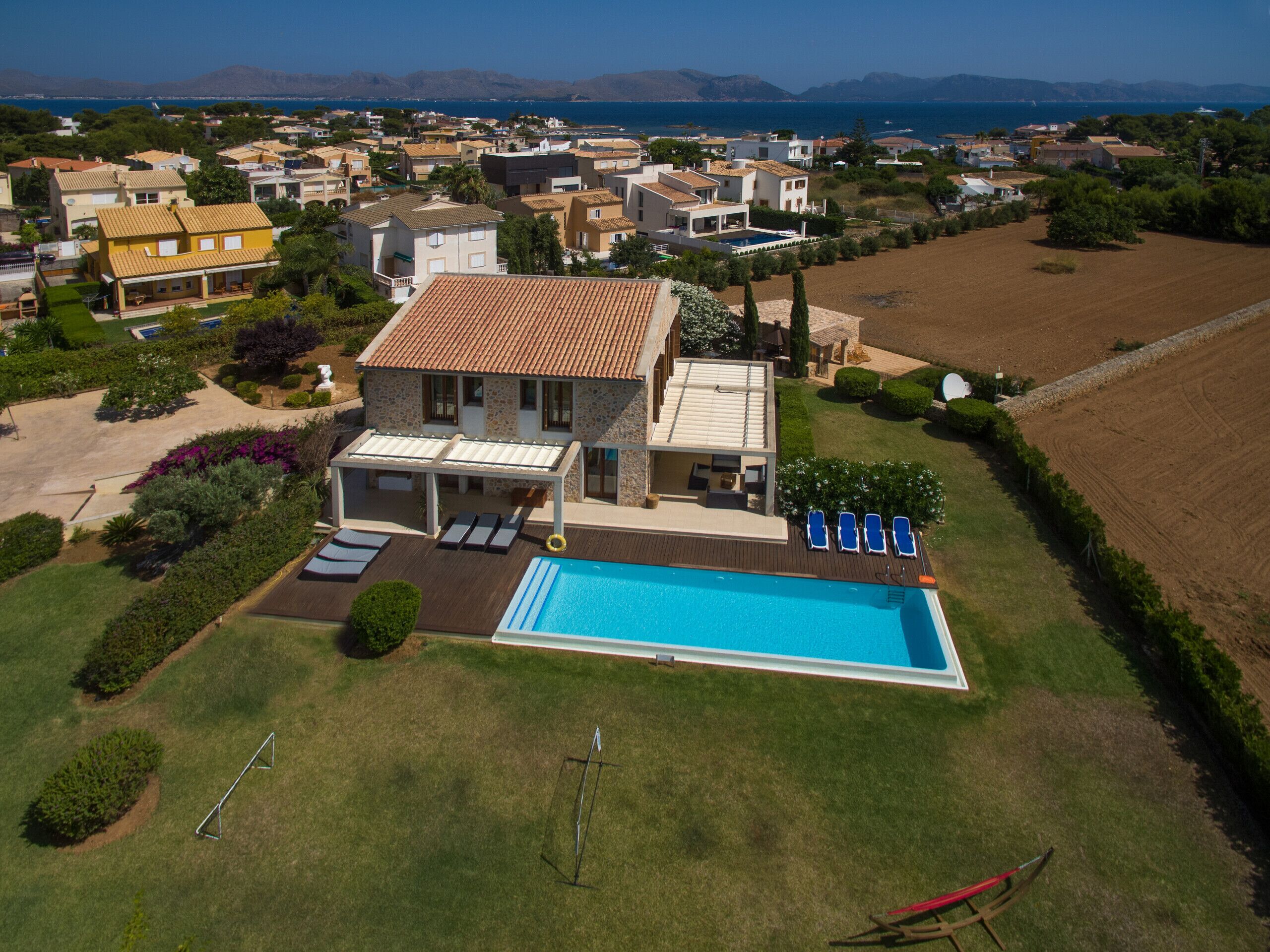 Une grande maison avec une piscine, entourée d’une pelouse bien entretenue et offrant une vue sur la mer.