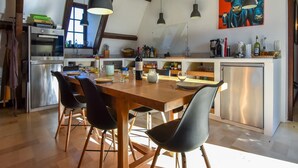 A modern kitchen with a wooden dining table, black chairs, pendant lights, and a painting of cows on the wall. - Pool Escape in Saint-Laurent (Saint-Laurent-la-Vallée)