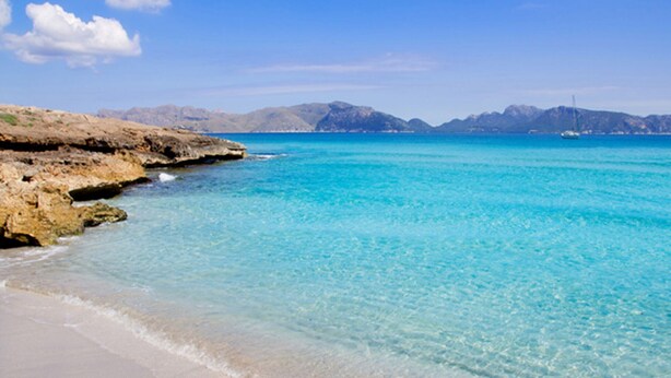 A beach with clear turquoise water, sandy shore, and rocky outcrops.