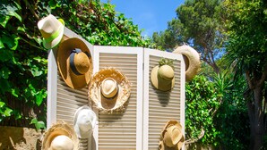 A white partition with multiple straw hats hanging on it, surrounded by greenery.