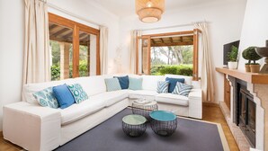 A modern living room with a white sectional sofa, two round coffee tables, a fireplace, and large windows with curtains.