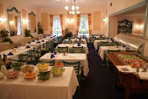 Un restaurante con varias mesas, sillas y una zona de bufé con distintos platos.