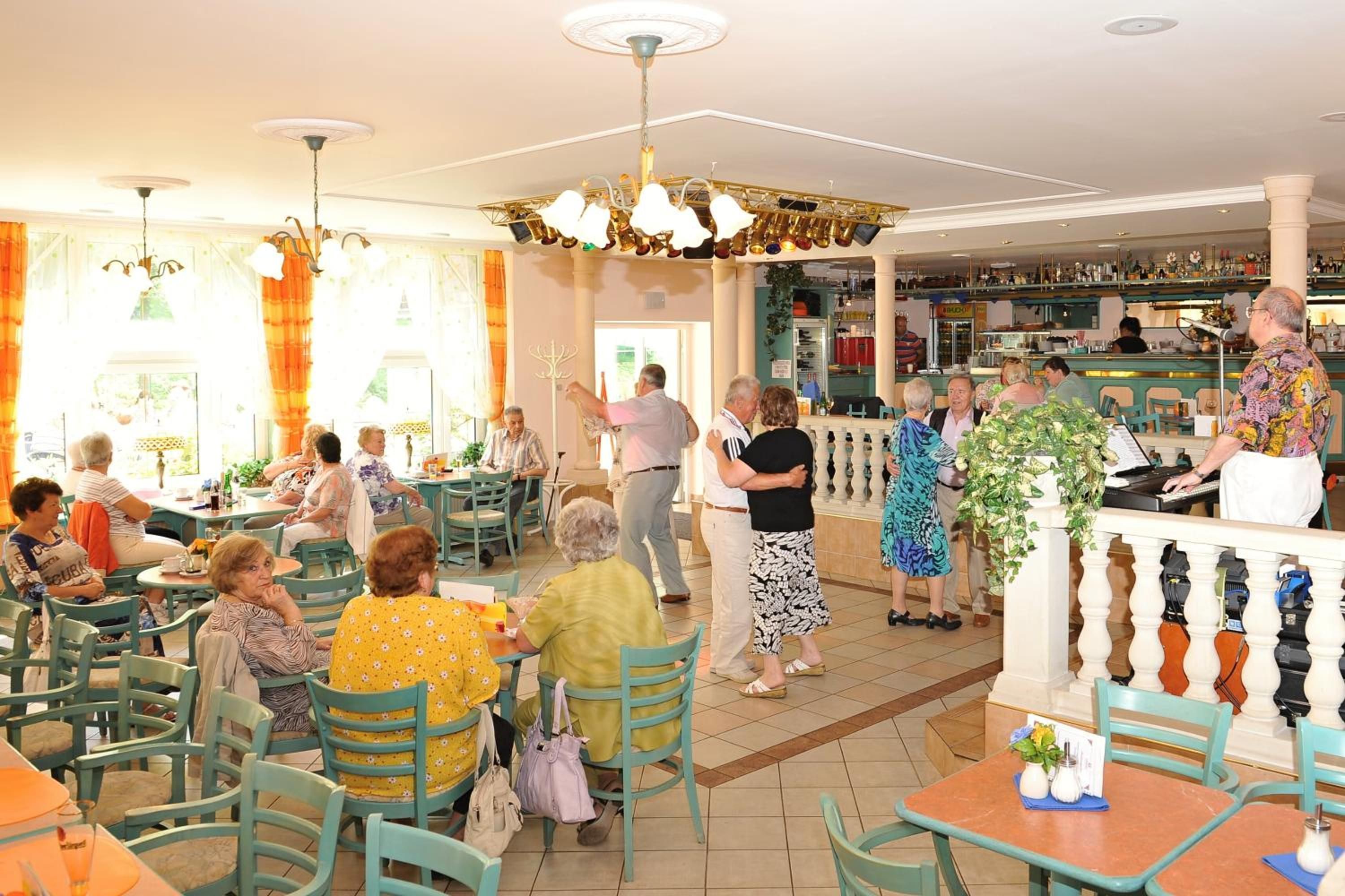Un restaurante con mesas en el interior, una zona de bar y varios comensales.