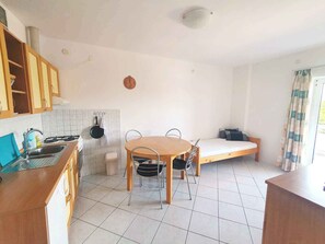 Une cuisine compacte avec une table et des chaises, un petit lit et une fenêtre avec des rideaux.