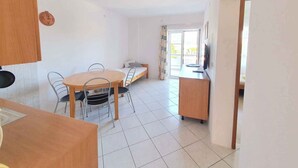 Una habitación con una mesa de comedor, sillas, un sofá, un televisor y un balcón al que se accede por un ventanal corredero.