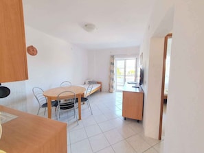 A room with a dining table, chairs, a sofa, a TV, and a sliding glass door leading to an outdoor area.