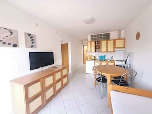 A modern kitchen with a dining area, a TV on a wooden cabinet, and a tiled floor.