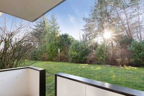 A view from a balcony overlooking a grassy yard with trees and a clear sky. - Apartment 13 (ID 368), Germany (Sankt Peter-Ording)