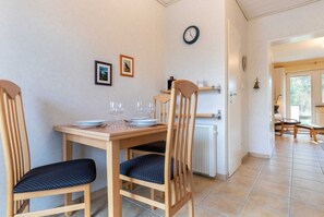 Un comedor con una mesa y sillas de madera, un reloj en la pared y vistas al exterior a través de una puerta.