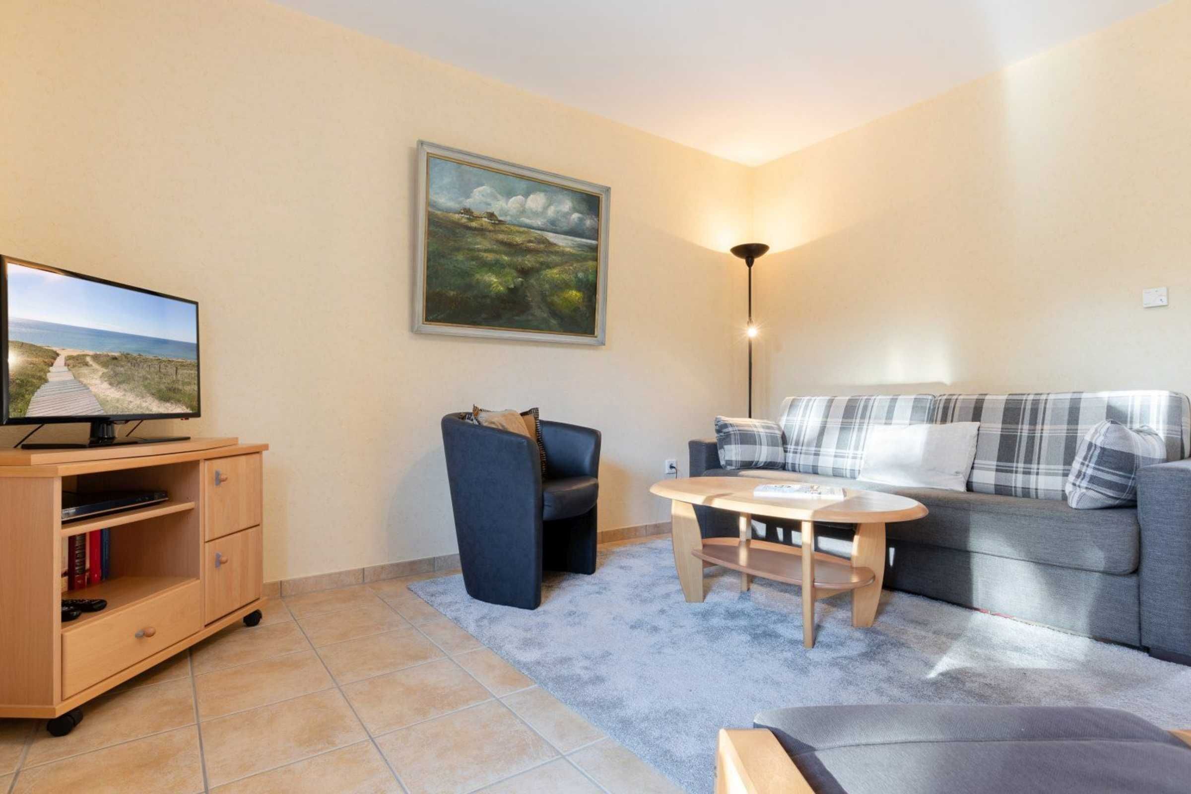 A living room with a sofa, a small table, a TV on a wooden cabinet, and a painting on the wall.