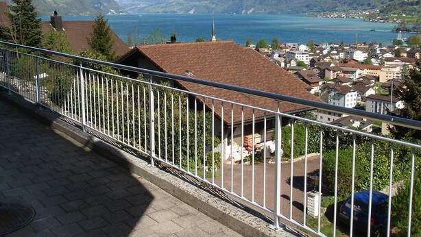 Un balcon doté d’une balustrade en métal, donnant sur une ville avec ses maisons et un lac.