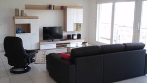 Un salon moderne avec un canapé noir, un fauteuil de bureau noir, un téléviseur à écran plat, une table basse et une bibliothèque.