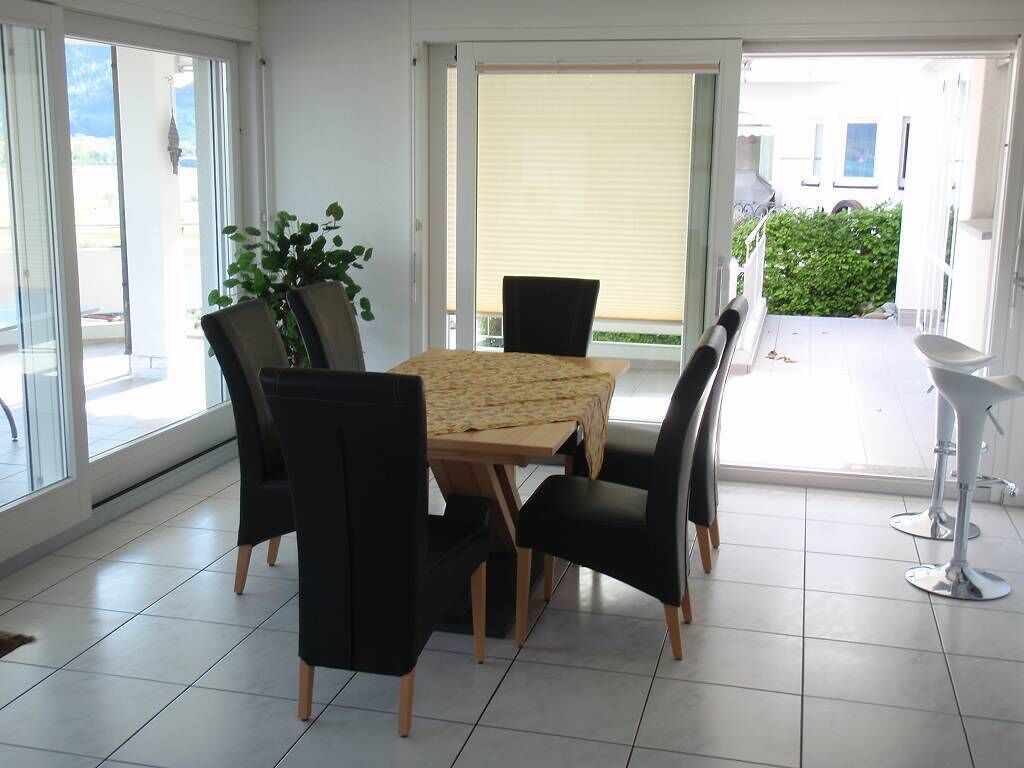 Un comedor con una mesa y sillas, una planta en maceta y vistas al exterior a través de un ventanal.