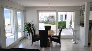Un espace repas moderne avec une table et des chaises, de grandes fenêtres et une vue sur l’extérieur.