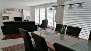 Un salon moderne avec une table à manger en verre, des chaises noires, un canapé noir, un téléviseur et une bibliothèque.