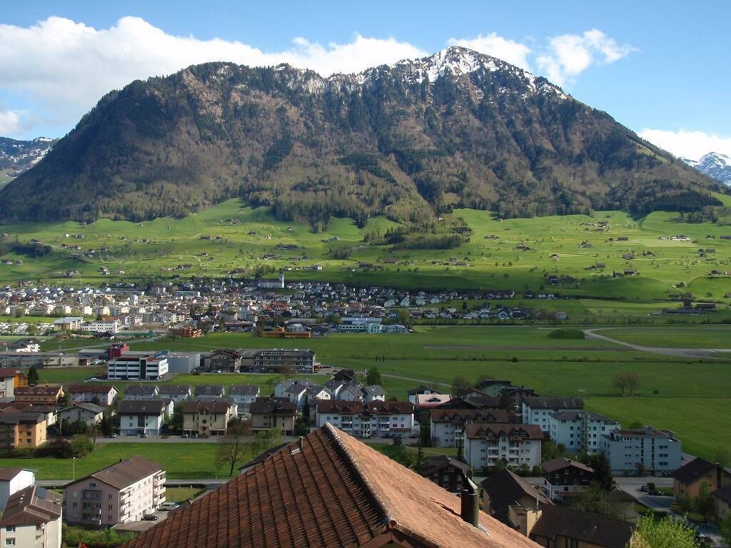 A town with a mountain backdrop, featuring residential buildings and a clear sky.