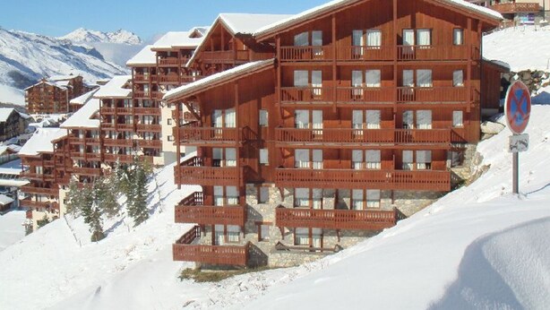 A multi-story wooden lodge with balconies, set against a snowy mountain backdrop.