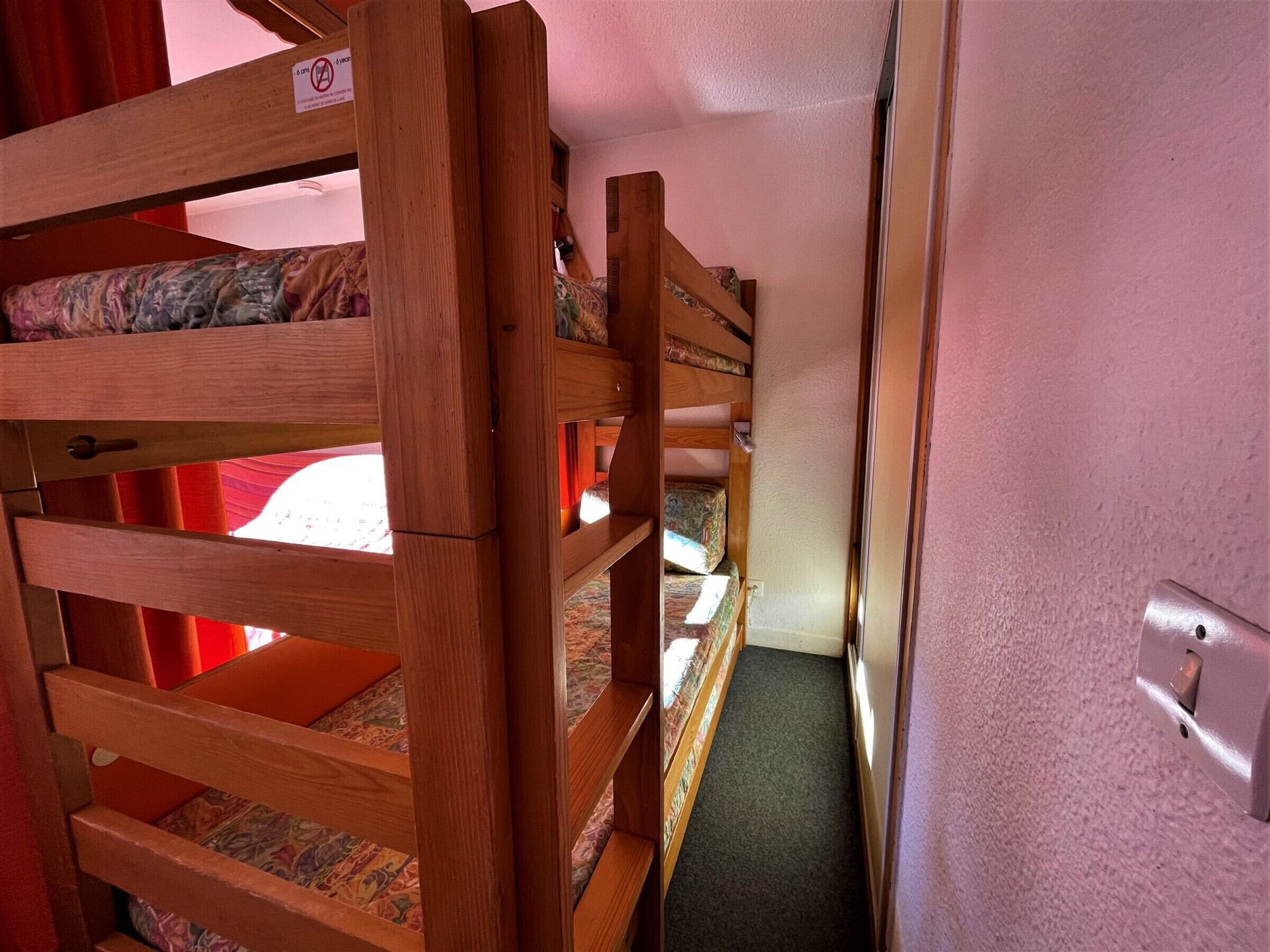 Ein Schlafraum mit Etagenbetten, einem Holzgestell, einem kleinen Fenster und einer Tür.