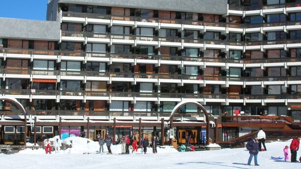Een hotel met meerdere verdiepingen, met een modern architectonisch ontwerp, voorzien van balkons en een skigebied op de voorgrond.