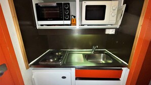 Een kleine keuken met een fornuis, magnetron en spoelbak.