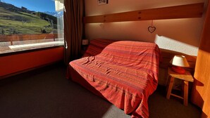 Een slaapkamer met een bed, een raam met uitzicht op een bergachtig landschap, een nachtkastje met een lamp en een hartdecoratie aan de muur.