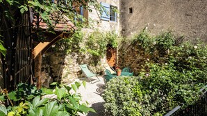 Un patio con un muro de piedra, un arco de madera y una pequeña área de jardín con una mesa y sillas.