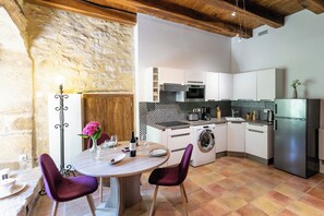 A compact kitchen with modern appliances, a dining table with chairs, and a stone wall.