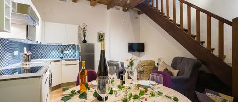 Een eethoek met een tafel voor vier personen, een keuken met een zwart-wit geruit spatwand, en een trap naar een hoger niveau.