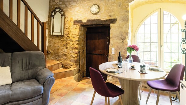 Una habitación con paredes de piedra, una escalera de madera, una mesa de comedor con sillas y un sofá.