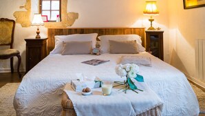 Una cama bien hecha con ropa blanca, una mesita de noche con una lámpara y una cesta de mimbre con cosas para el desayuno.
