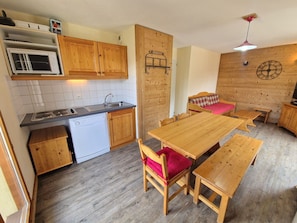 A compact kitchen with wooden cabinets, a built-in stove, and a dishwasher. There is a dining area with a wooden table and benches.