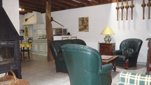 Un salon avec une cheminée, deux fauteuils en cuir vert, une table et une lampe.