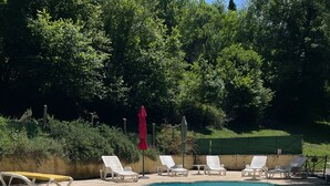 Une piscine rectangulaire à l’eau d’un bleu cristallin, entourée de chaises longues blanches et agrémentée d’un parasol rouge.