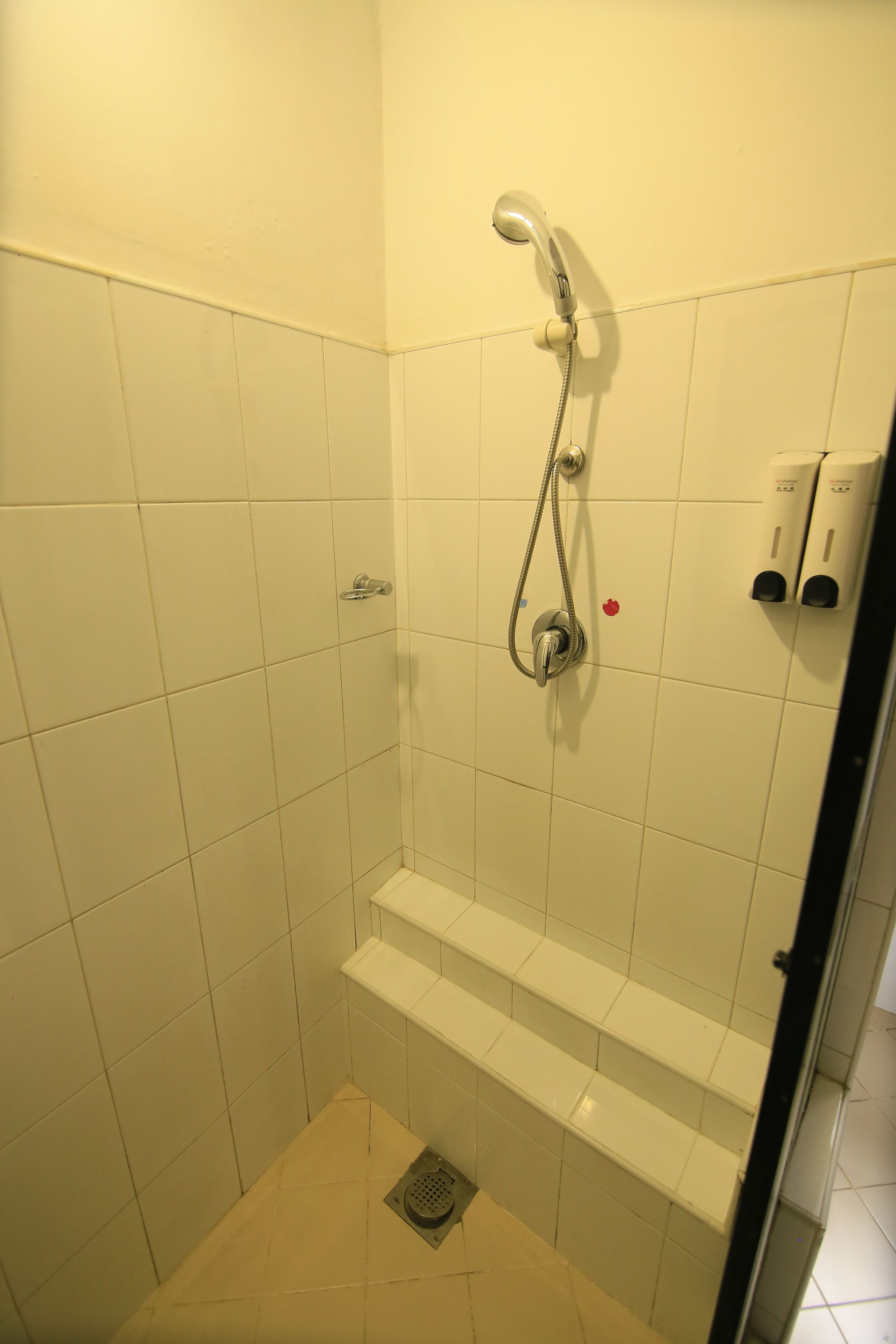 A small, tiled shower stall with a handheld showerhead and a built-in seat.