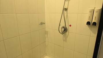A small, tiled shower stall with a handheld showerhead and a built-in seat.