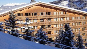 A wooden chalet with multiple balconies, surrounded by snow-covered trees and mountains.
