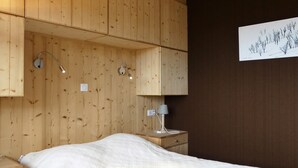 A bedroom with a bed, wooden panel walls, a nightstand, a lamp, and a wall-mounted artwork.