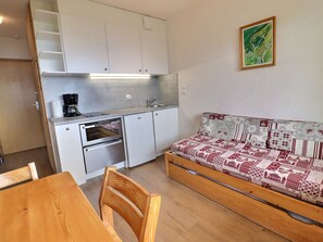 A compact kitchenette with a coffee maker, a sink, and a stove. There is a wooden dining table with chairs and a sofa with patterned cushions.
