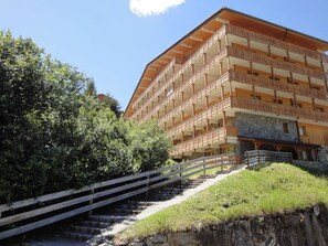 A multi-story building with balconies, a stone base, and a wooden staircase leading up to the entrance.