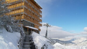 A multi-story hotel with balconies, a staircase leading up to the entrance, and a mountainous backdrop. - Cozy 2-room apartment in Méribel, 1 bedroom, for 3 people (Méribel)