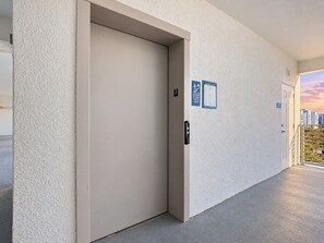 A hallway with a closed elevator door, a fire exit sign, and a door with a number plate.