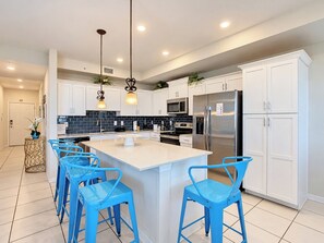 A modern kitchen with white cabinets, a central island, blue bar stools, stainless steel appliances, and pendant lighting. - Amazing stay/Waterpark/Near Disney (Kissimmee)