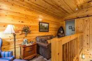 Una habitación acogedora con paredes de madera, un sofá de cuero marrón, una silla azul a rayas, un aparador de madera y una lámpara.