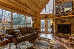 Interior acogedor de una cabaña con chimenea de piedra, un sofá de cuero y un televisor montado encima.