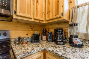 A kitchen with wooden cabinets, a granite countertop, a toaster, a coffee maker, a blender, and a microwave.