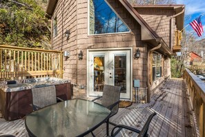 A wooden deck with a glass table and chairs, a hot tub, and a stone fireplace.