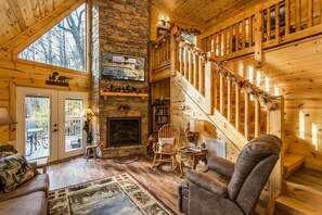 Interior acogedor de una cabaña con chimenea, escalera de madera y un ventanal con vistas a una terraza.