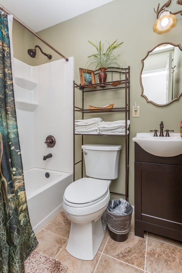 Un baño con inodoro blanco, una bañera, un lavabo con espejo y un estante con toallas y una planta.